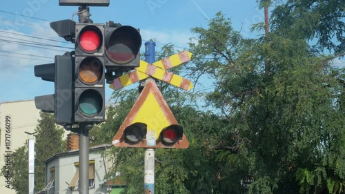 A red light on a traffic light for vehicles and old sign next to it with two flashing red lights signaling that a train is coming