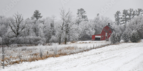 Old red weathered barn in snow covered trees on the farm