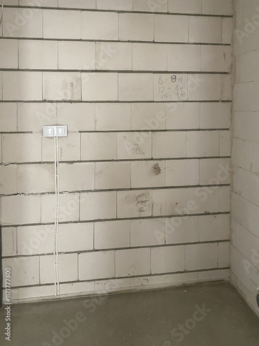 Empty brick wall with two electrical sockets, flat in the process of renovation from the builder, floor with concrete screed 