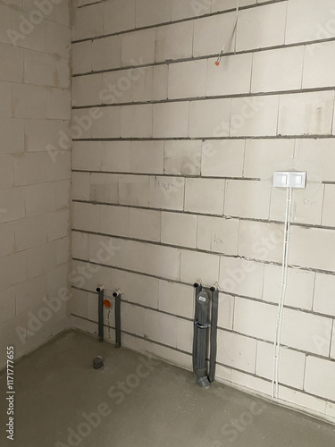 Empty bathroom from builder with water connection for washbasin and bath, bare walls in the process of renovation 