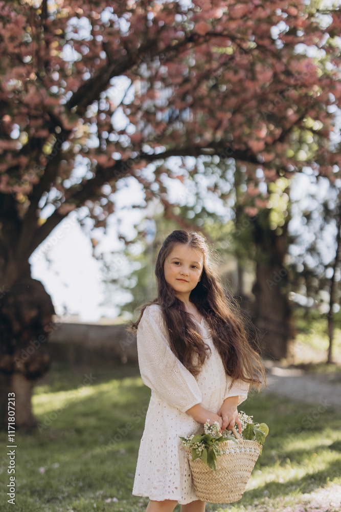 Young girl holding flowers in basket under blooming tree in spring Young girl holding flowers in basket under blooming tree in spring