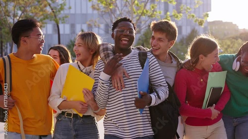 Group of generation z international university students laughing walking hugging together on campus. Young diverse people looking surprised at each other holding backpacks and workbooks outdoors