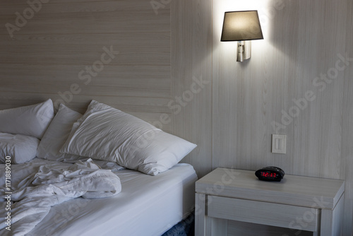 Unmade bed on one side Alarm clock on a dresser under a lamp photo