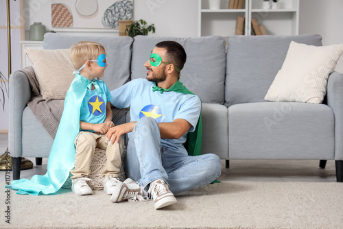 Happy father with his little son dressed as superheroes sitting at home photo