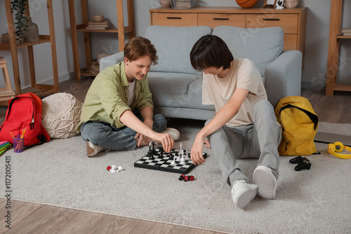 Male students playing chess on carpet at home photo