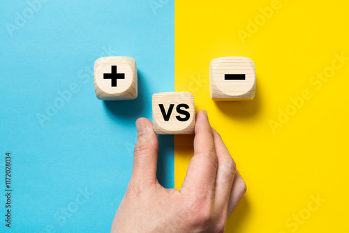 Картината върху платно Hand placing a wood block versus between plus and minus sign on blue and yellow