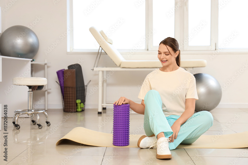 Female physiotherapist with foam roller sitting on mat in rehabilitation center Female physiotherapist with foam roller sitting on mat in rehabilitation center