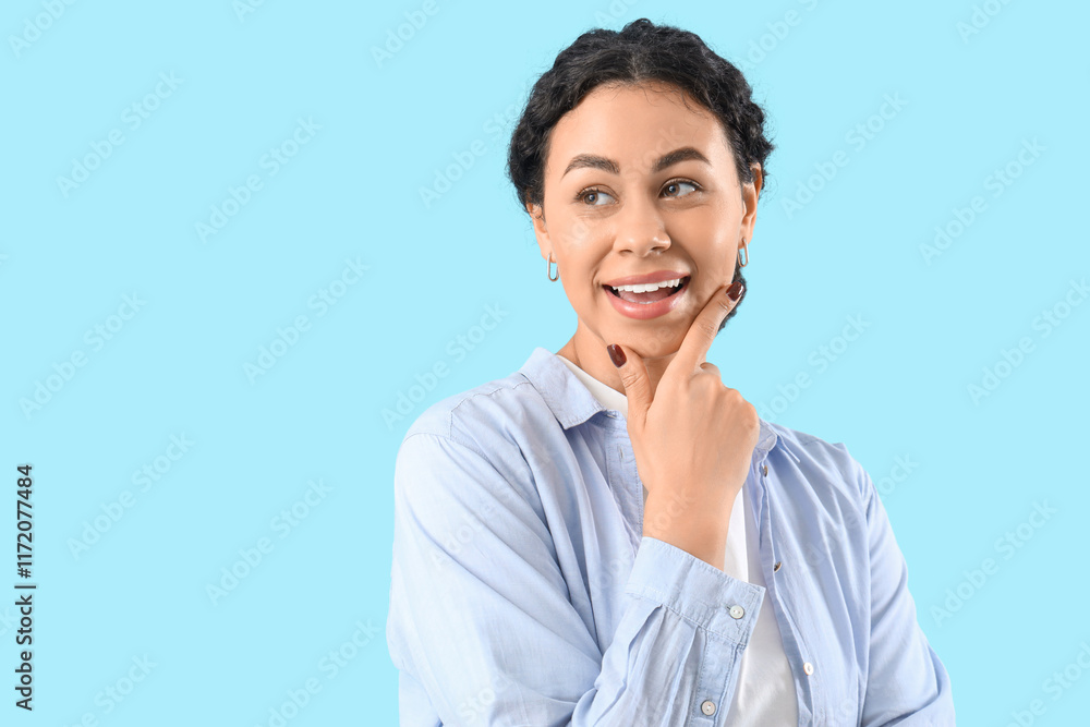 Thoughtful young African-American woman smiling on blue background, closeup Thoughtful young African-American woman smiling on blue background, closeup