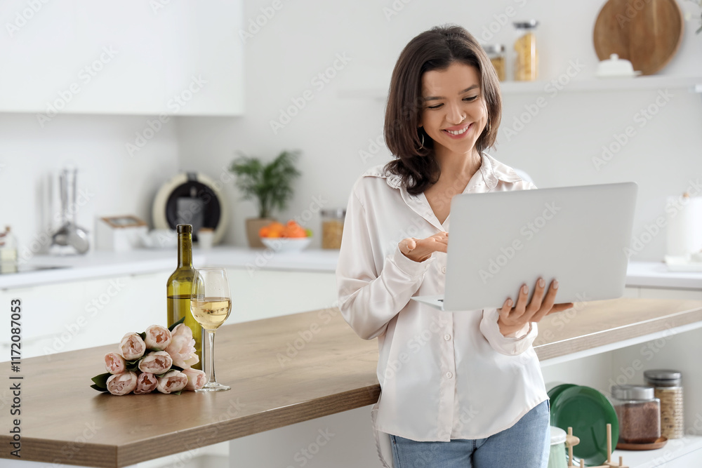 Young woman with laptop having online date in kitchen Young woman with laptop having online date in kitchen