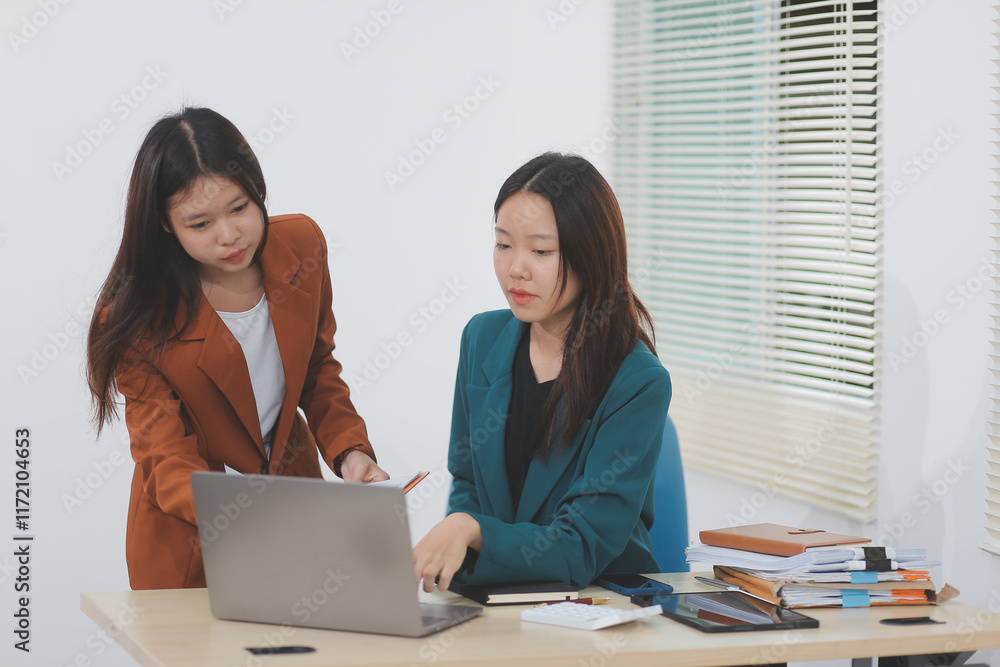 Two young Asian businesswoman discuss investment project working and planning strategy. Business people talking together with laptop computer at office. Two young Asian businesswoman discuss investment project working and planning strategy. Business people talking together with laptop computer at office.
