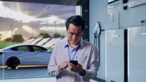 Wallpaper Mural Asian Male Professional Worker Standing With His Smartphone With Home Energy Storage System In a Modern Garage, Work Continuously On His Device Torontodigital.ca