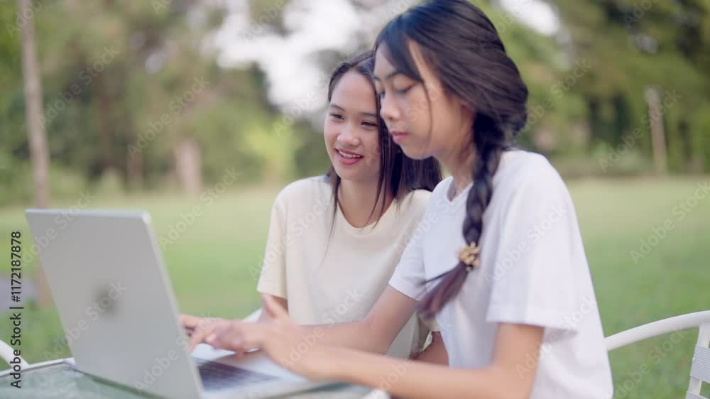 Two women sitting on a bench looking at a laptop. One of them is typing. Scene is friendly and relaxed Two women sitting on a bench looking at a laptop. One of them is typing. Scene is friendly and relaxed