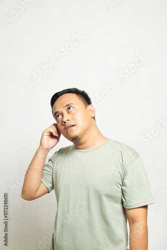 portrait of the body of an adult male holding his ear with his hand while wearing sage clothing.