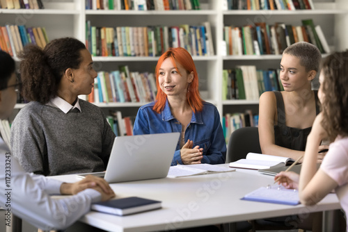 Got an idea. Attentive diverse group of polyethnic high school students college pupils learn together at desk in library listen to smart red haired female teammate offer research plan explain subject