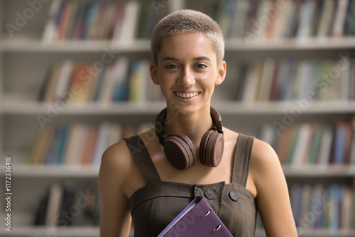 Smart and stylish. Head shot portrait smiling teen female student in casual clothing with trendy short ashy blond hair wear casual clothes modern wireless headset around neck look at camera in library photo