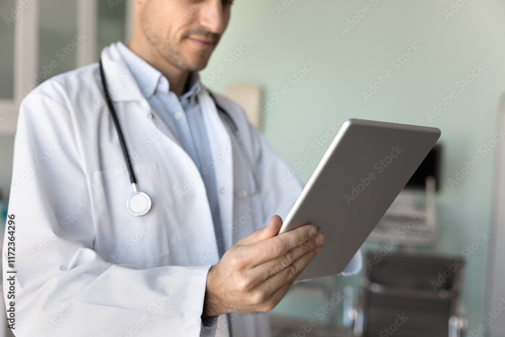 Male physician doctor in white coat using modern technology, working with tablet in hospital office, reading patients history records, medical examination electronic reports. Cropped shot Male physician doctor in white coat using modern technology, working with tablet in hospital office, reading patients history records, medical examination electronic reports. Cropped shot