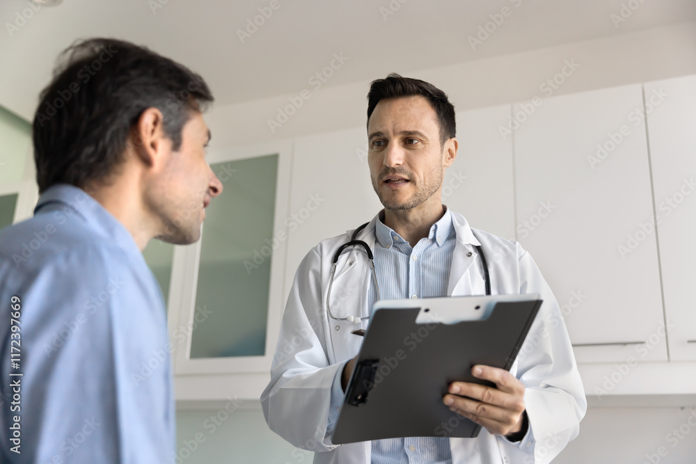 Serious general practitioner, cardiologist man talking to patient in clinic office, asking man about complaints, writing notes in paper records, giving consultation, prescription, recommendation Serious general practitioner, cardiologist man talking to patient in clinic office, asking man about complaints, writing notes in paper records, giving consultation, prescription, recommendation