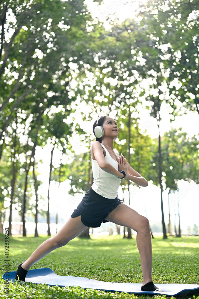 Serene African American woman wearing headphones practicing yoga on mat in a park Serene African American woman wearing headphones practicing yoga on mat in a park