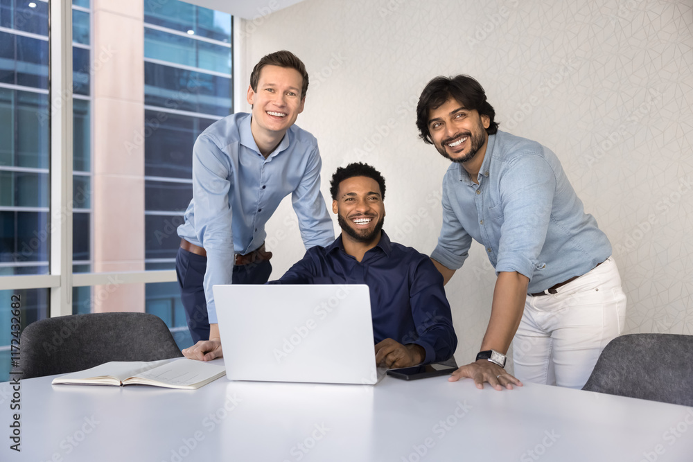 Casual portrait of happy male business colleagues meeting at laptop for teamwork, cooperation, having fun, laughing, smiling, looking away, sitting and standing at large office table Casual portrait of happy male business colleagues meeting at laptop for teamwork, cooperation, having fun, laughing, smiling, looking away, sitting and standing at large office table