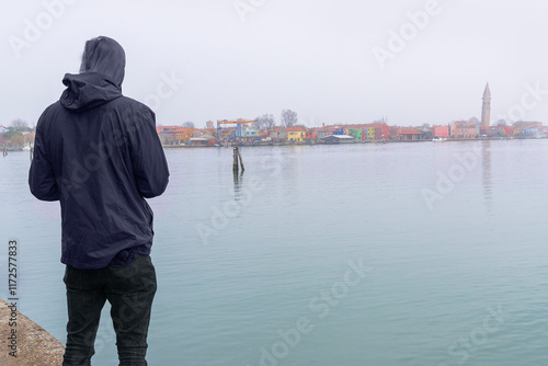 Young Traveler Observing Burano Coastline from Mazzorbo with Colorful Houses and Leaning Tower of San Martino photo