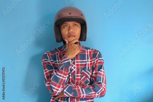 Young Asian man wearing motorbike helmet showing thinking expression
