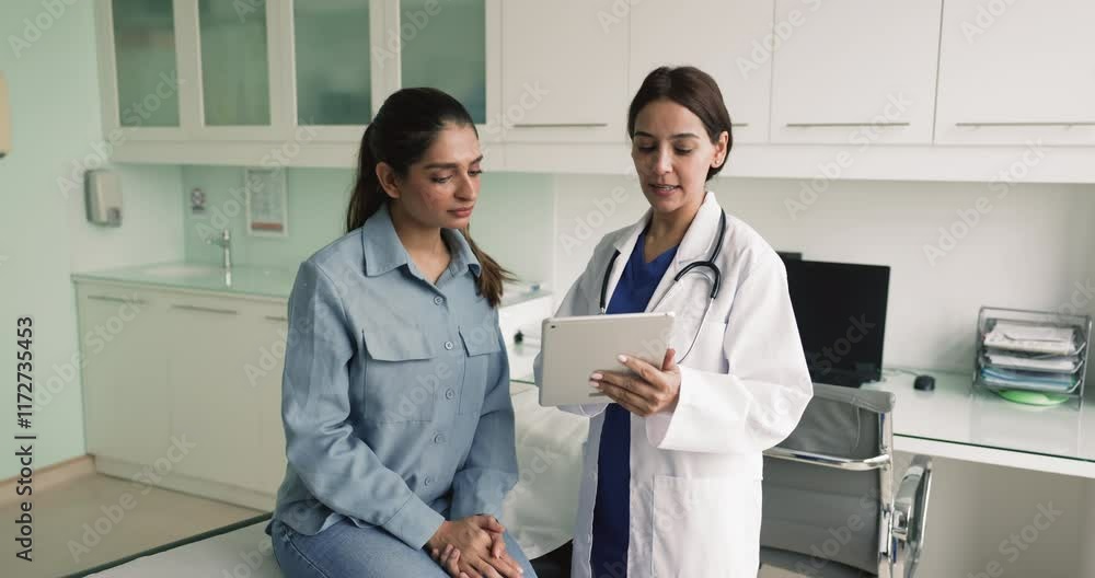 Young Middle Eastern doctor woman talking to female patient in clinic office, showing examination results on tablet explaining image, diagnosis, treatment, recommendation Young Middle Eastern doctor woman talking to female patient in clinic office, showing examination results on tablet explaining image, diagnosis, treatment, recommendation