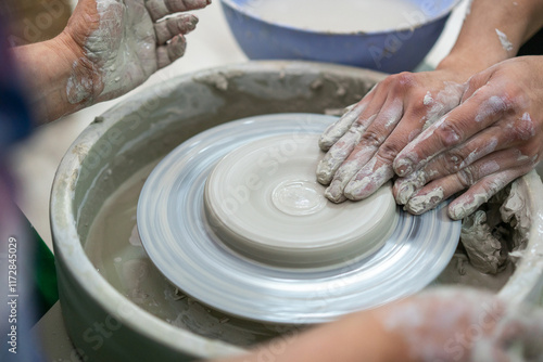 Close-up of hands covered in wet clay as two people collaboratively shape a pottery piece on a spinning wheel, emphasizing the teamwork and artistry involved in ceramic craftsmanship. photo