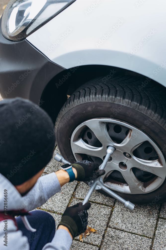 Man changing his car's tire with a wrench, replacing it with winter tires for the season Man changing his car's tire with a wrench, replacing it with winter tires for the season