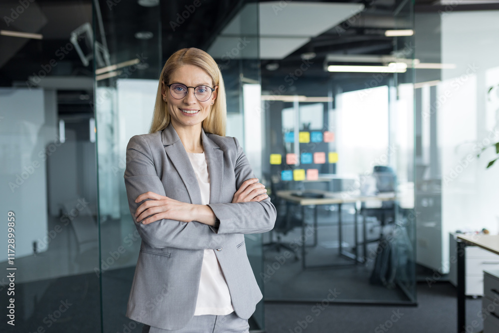 Obraz premium Portrait of confident successful woman inside office at workplace. Businesswoman in business suit with crossed arms smiling and looking at camera.