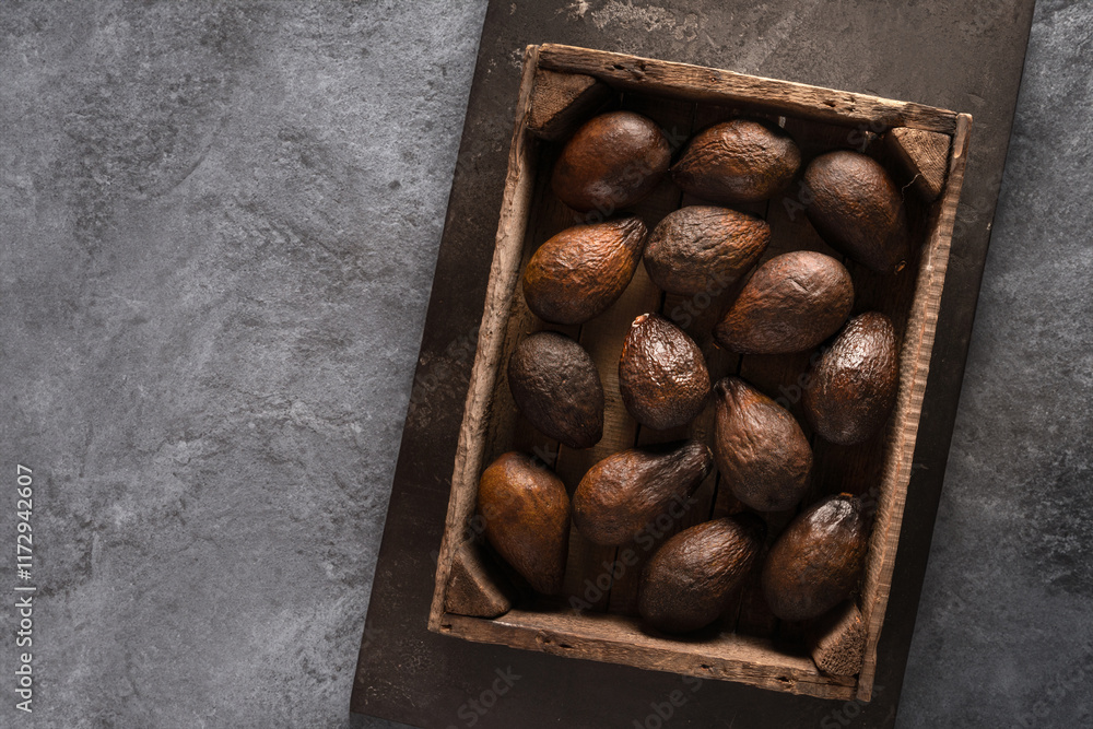 Fototapeta premium Top view of an old brown avocado in a wooden box. The concept of aging, storage and spoilage of fruits, as well as a beautiful textured background.