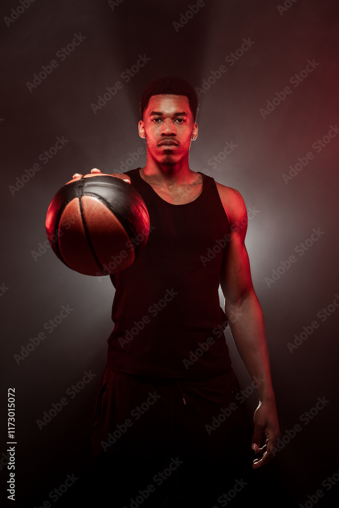 Basketball player side lit with red color holding a ball against hazy smoke fog background. Serious concentrated african american man. Basketball player side lit with red color holding a ball against hazy smoke fog background. Serious concentrated african american man.