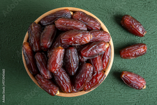 Large dates fruit in a wooden bowl on green background
