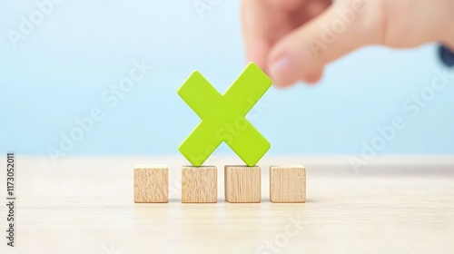 A hand places a green cross shape atop wooden blocks, symbolizing decision-making or evaluation in a minimalist, light-colored setting. photo