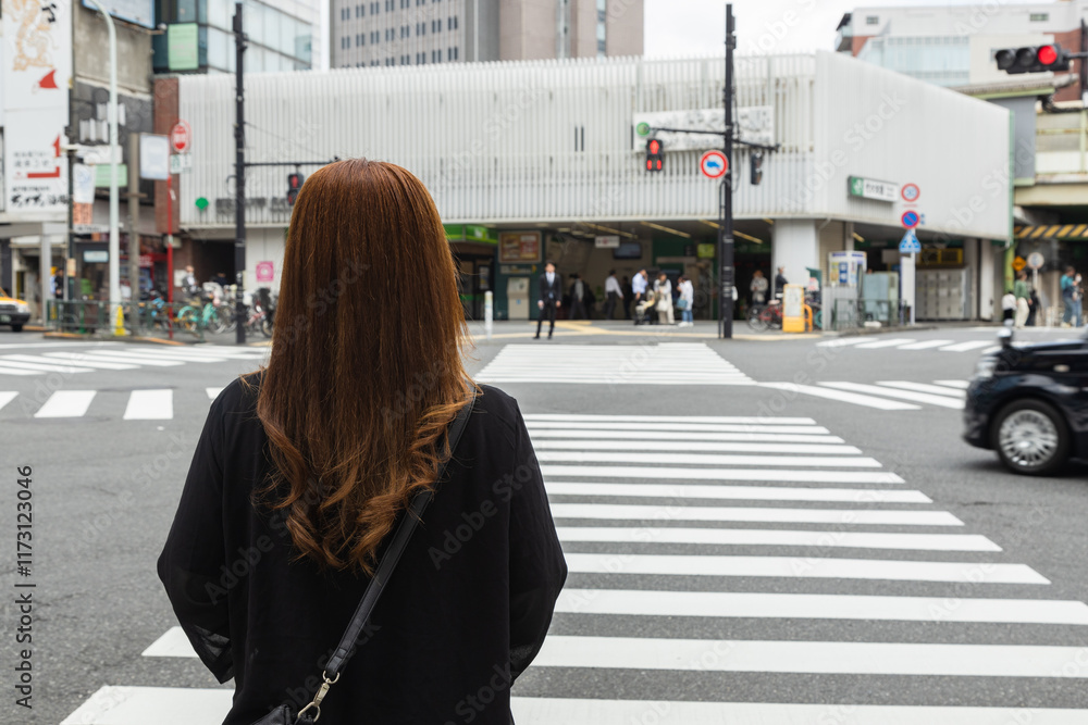 A woman waiting at the pedestrian pathway to cross a street in Tokyo, Japan, on her way to the train station to commute to work