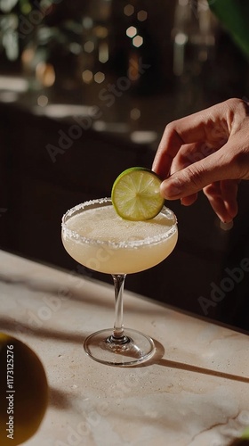 Bartender garnishes Margarita with a fresh lime slice at a lively bar photo