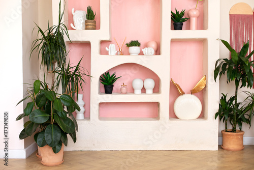 Stylish interior of wabi sabi style living room with design shelf with home decoration and plants in pots. Modern home decor. Collection of cacti in pots on shelf. Green ficus in terracotta pot.	
