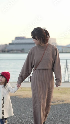 In December 2024, a Japanese parent and child (a 3-year-old girl and her 30s mother) spend the evening at a park near the sea in Fukuoka. Vertical slow motion video.