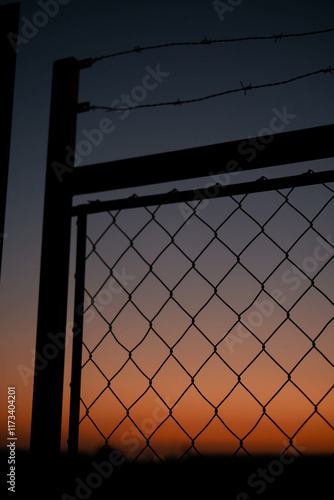 Silhouette of a metal fence with barbed wire at dusk photo