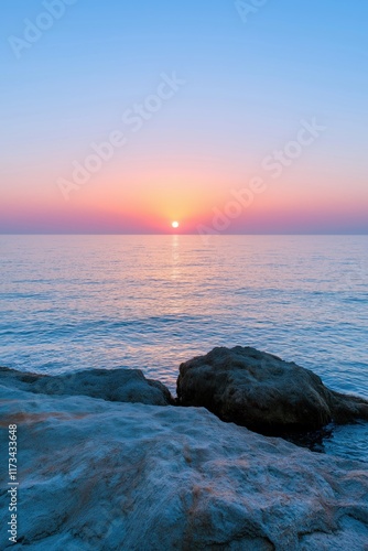 A beautiful sunset over the ocean with a rock in the foreground. The sky is a mix of blue and pink, and the water is calm. The rock adds a sense of stability and permanence to the scene photo