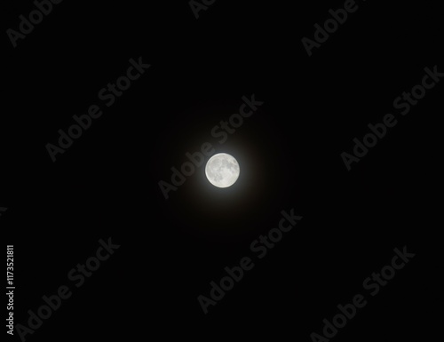 Bright full moon on pitch black night sky, glowing white