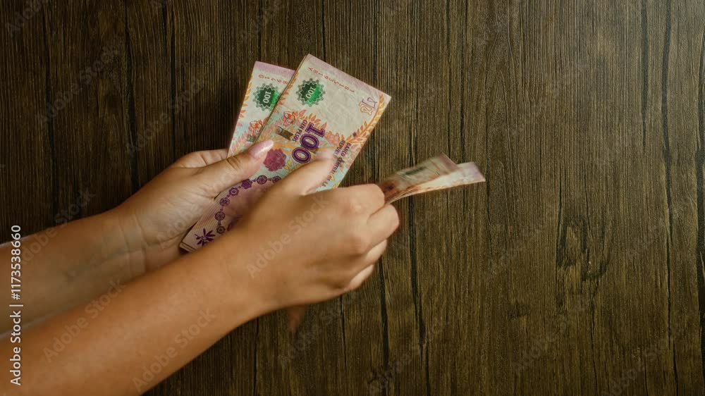 Woman counting argentinian pesos with her hands on a wooden background, highlighting details of currency from argentina including hands, fingers, and money. Woman counting argentinian pesos with her hands on a wooden background, highlighting details of currency from argentina including hands, fingers, and money.