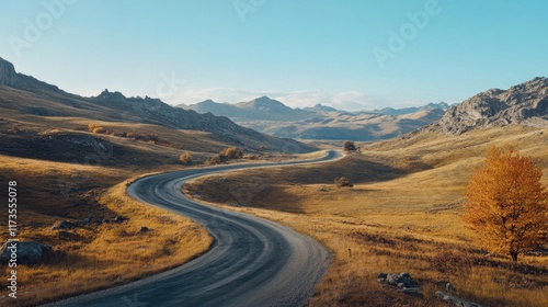 A winding mountain road captured during autumn, with vibrant fall foliage, rolling hills, and a clear blue sky above, inviting travelers to explore naturea??s beauty.  photo