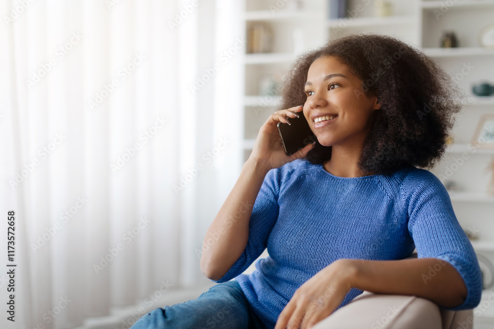 Smiling african american woman sitting on a couch engaged in a phone conversation on a mobile device, happy african american female talking on cellphone at home. High quality photo Smiling african american woman sitting on a couch engaged in a phone conversation on a mobile device, happy african american female talking on cellphone at home. High quality photo