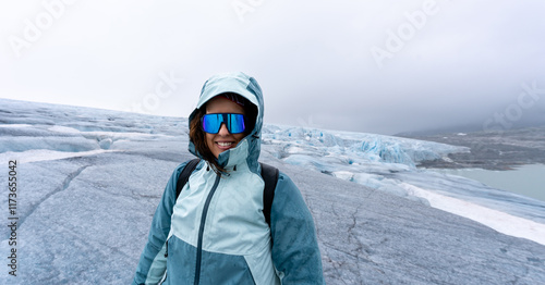 Portrait of a brunette woman in her 30s, looking at camera smiling, dressed in mountaineering gear, stands on the unspoiled icy expanse of Austdalsbreen Glacier in Jostedal, Norway