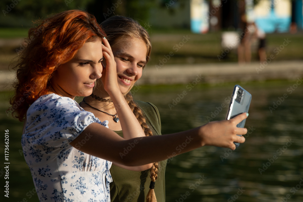 Two friends happily take a selfie by calm water at sunset, capturing their joyful connection Two friends happily take a selfie by calm water at sunset, capturing their joyful connection