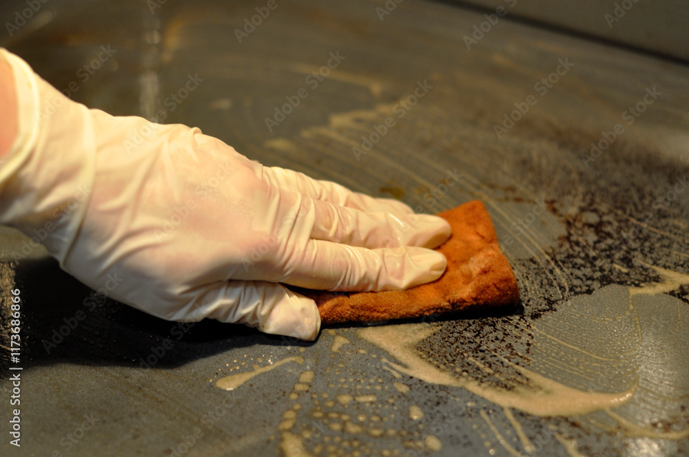 Φωτογραφία A woman's hand in a latex protective glove washes a dirty oven with a sponge