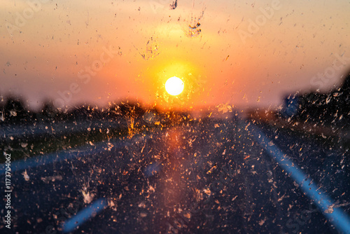 Blurry highway through a smudged dirty car windshield,  affecting visibility during sunset, emphasizing highway traffic safety concerns and the importance of clean glass for safe travel.  
