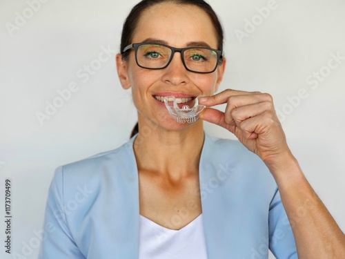 Smiling woman demonstrating clear dental aligner in a bright, neutral setting during a dental consultation photo