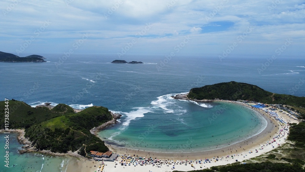 Naklejka premium Aerial drone view of Conchas Beach (praia), Cabo Frio, Rio de Janeiro, Brazil. The beach’s unique shell-like shape stands out, surrounded by clear Atlantic Ocean waters and stunning natural scenery.