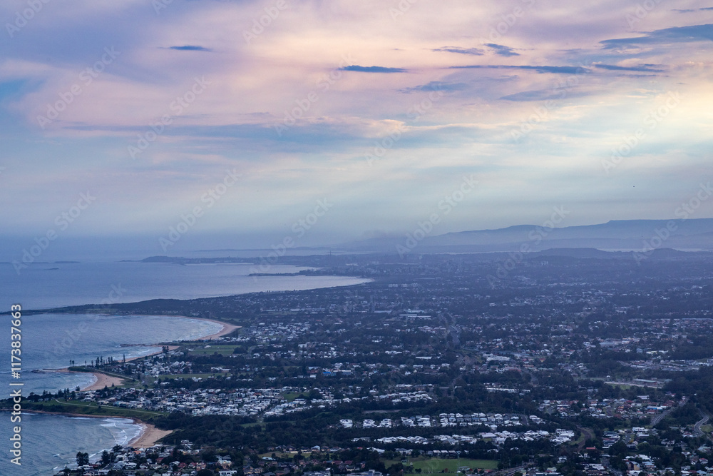 Obraz premium A scenic aerial view of a coastal city nestled along the shoreline. The city meets the ocean, with beaches, cliffs, and urban development visible. Rolling hills or mountains are visible in the distanc